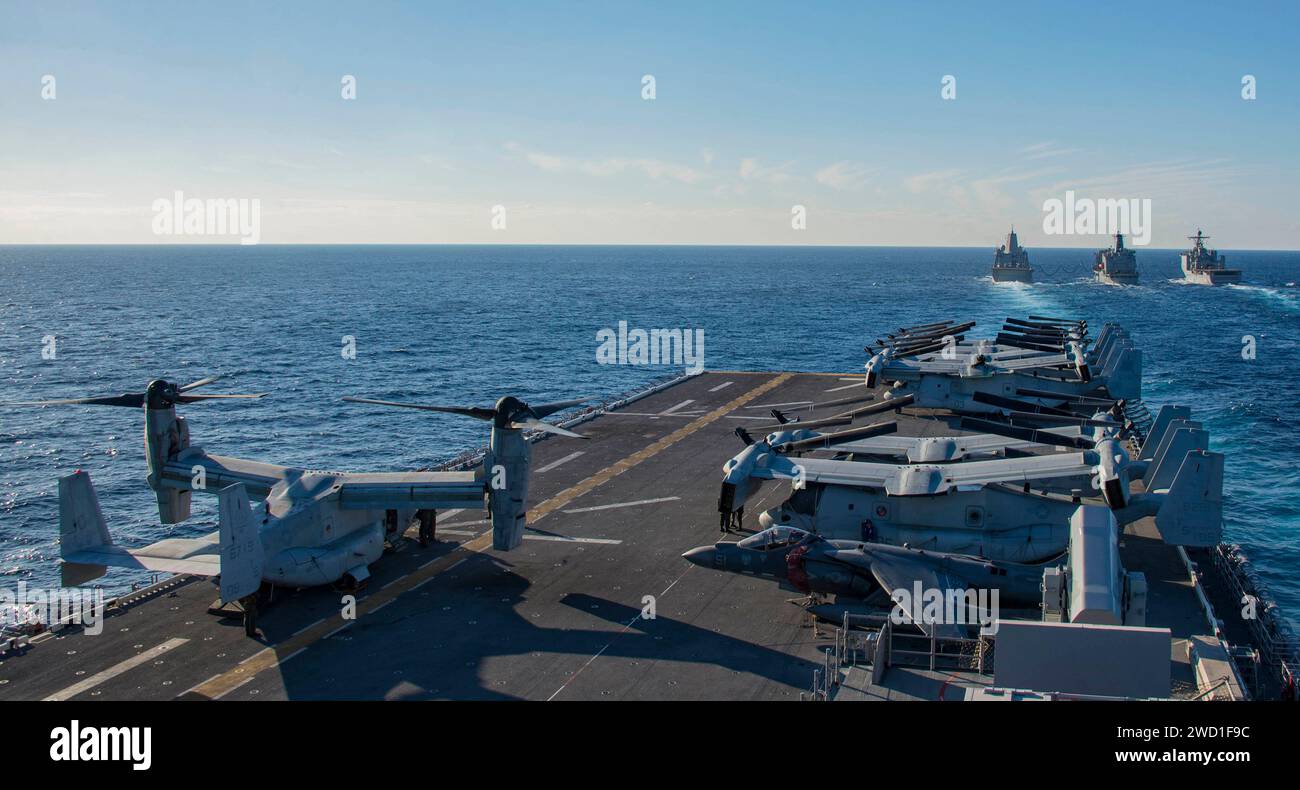 Aircraft aboard USS Iwo Jima transit behind a group of U.S. Navy ships conducting a replenishment at sea. Stock Photo