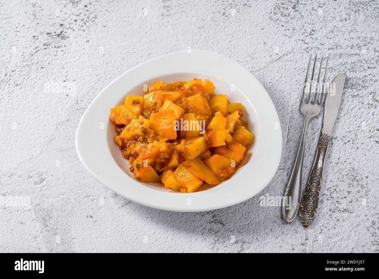 Minced meat and potato dish on white porcelain plate on stone table Stock Photo