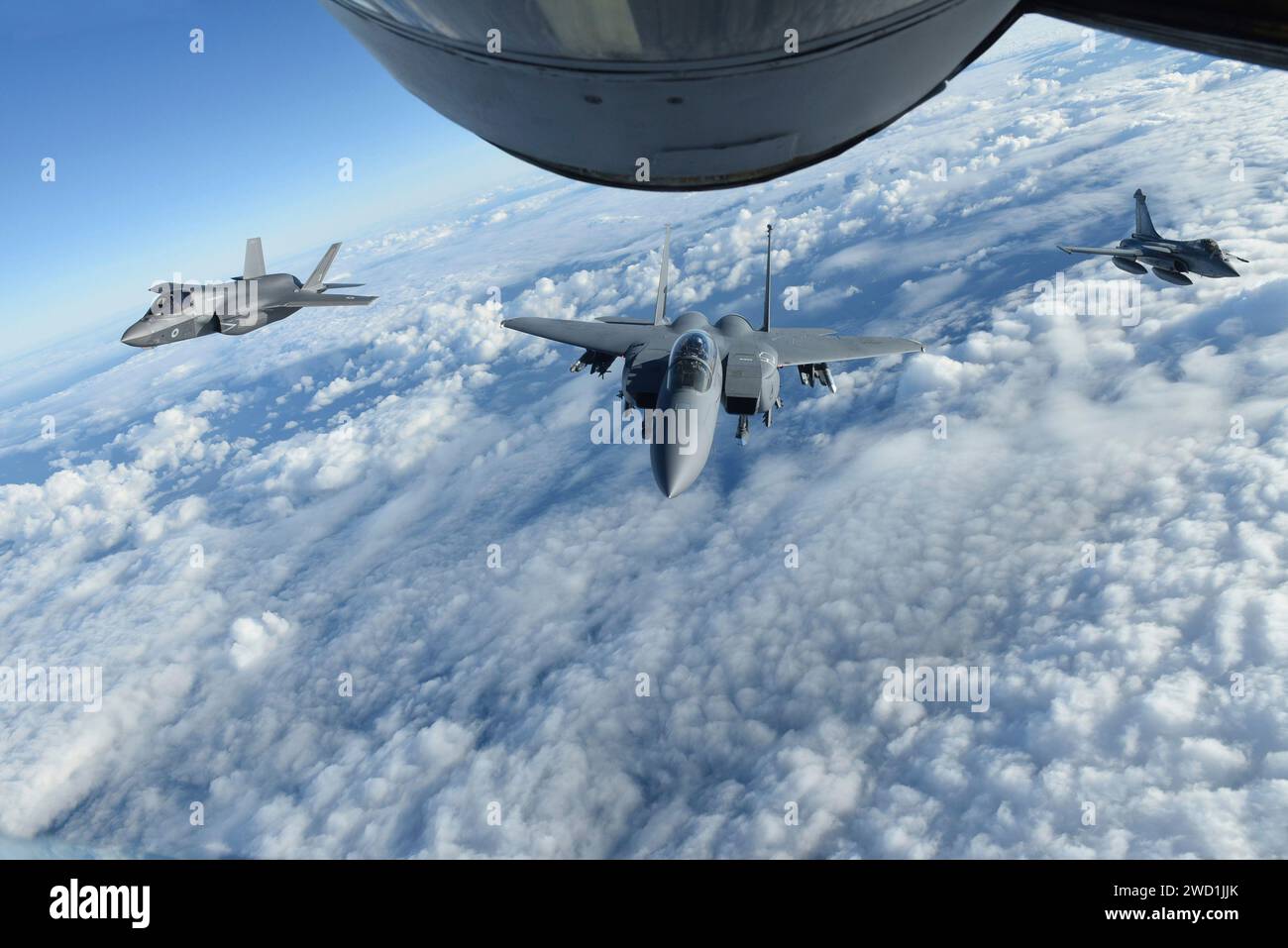 A Royal Air Force F-35 Lightning II, U.S. Air Force F-15E Strike Eagle and French Air Force Rafale fly behind a  KC-135 Stratotanker. Stock Photo