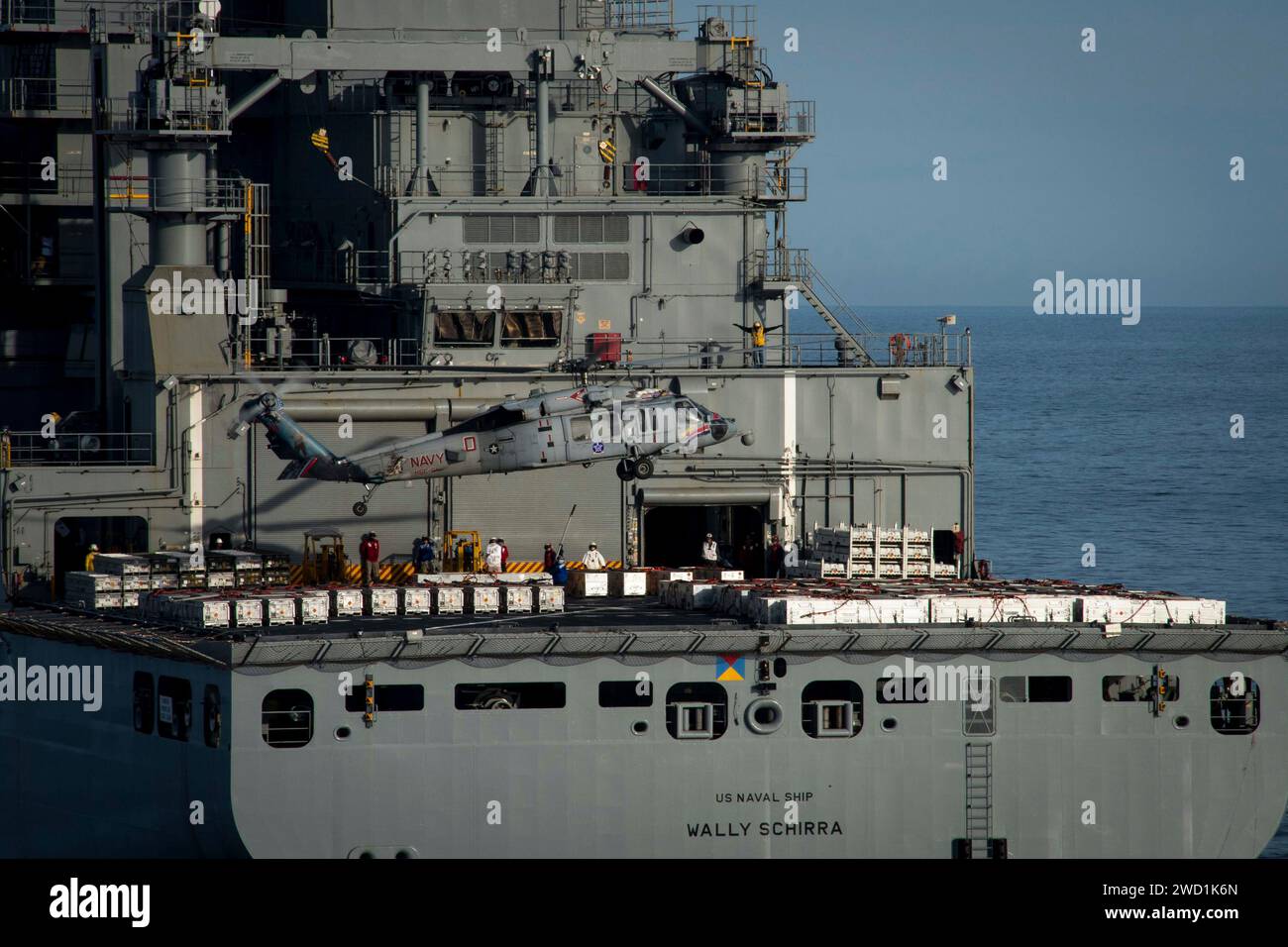 An MH-60S Sea Hawk helicopter picks up ordnance from the flight deck of USNS Wally Schirra. Stock Photo