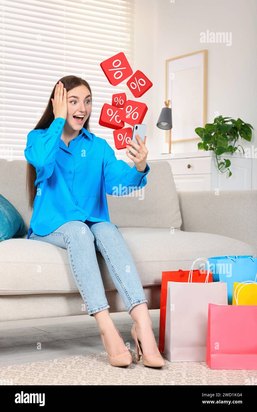 Discount offer. Shocked woman with mobile phone at home. Percent signs flying out of device Stock Photo