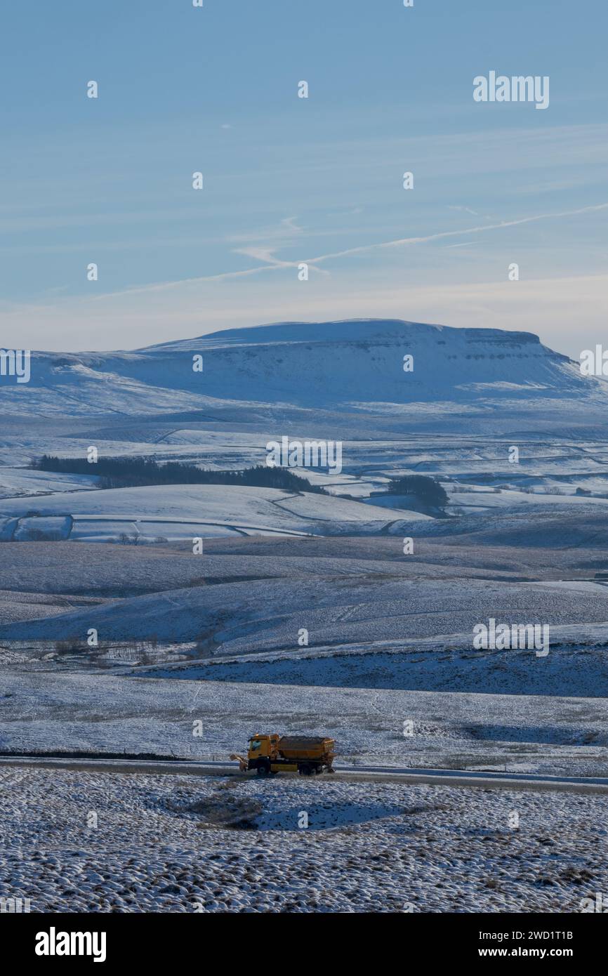 A gritter lorry gritting the roads on a beautiful winter day in the Yorkshire Dales National Park in England, with Pen-y-ghent in the background. Stock Photo