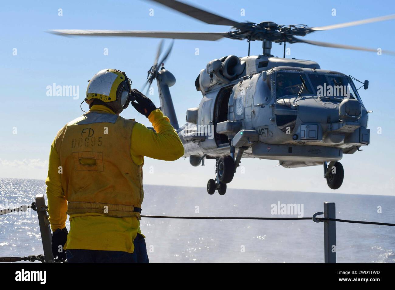 Boatswain's Mate signals to an MH-60R Sea Hawk helicopter during a vertical replenishment. Stock Photo