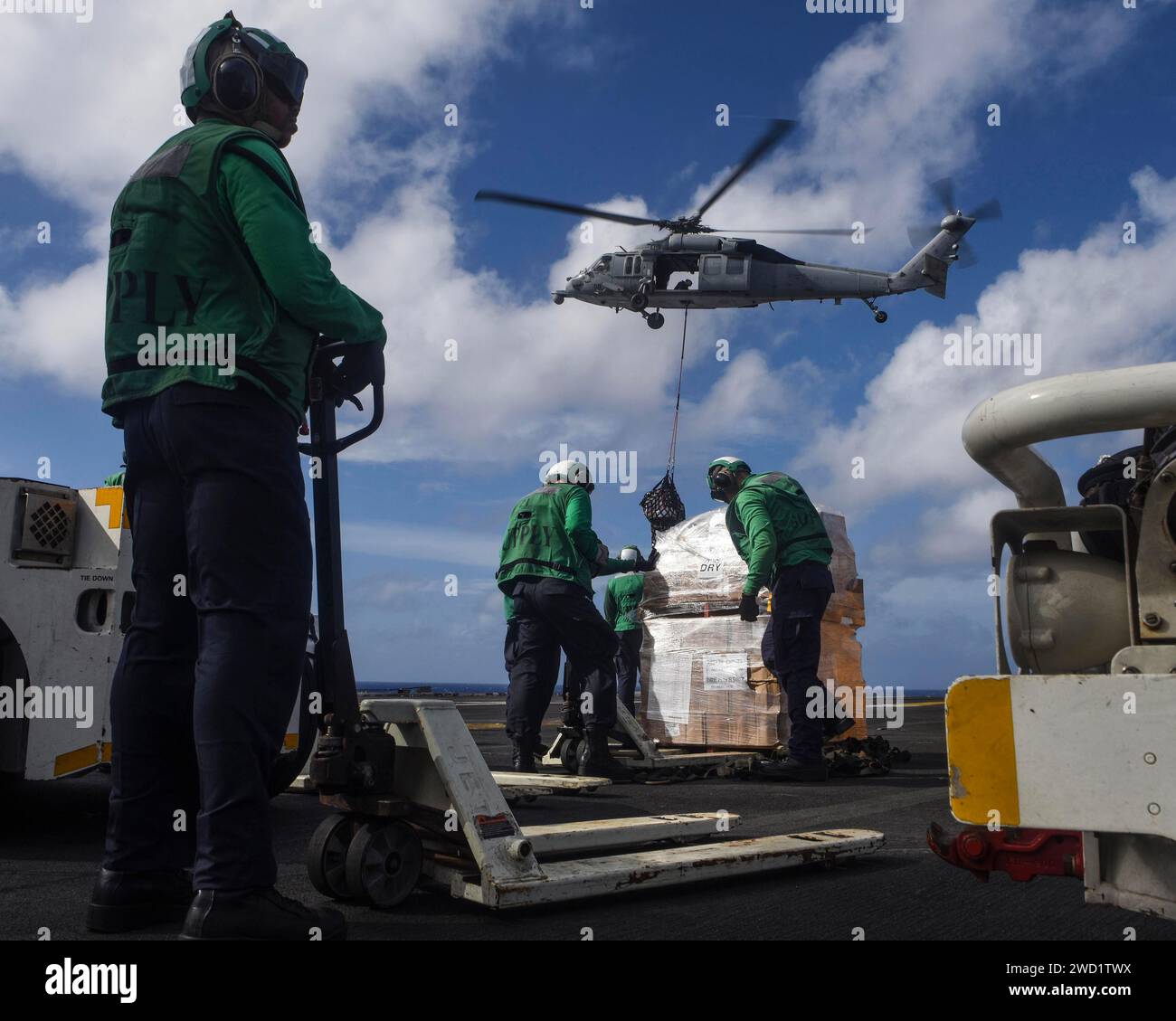 Sailors retrieve cargo delivered by an MH-60S Sea Hawk helicopter during a replenishment-at-sea. Stock Photo