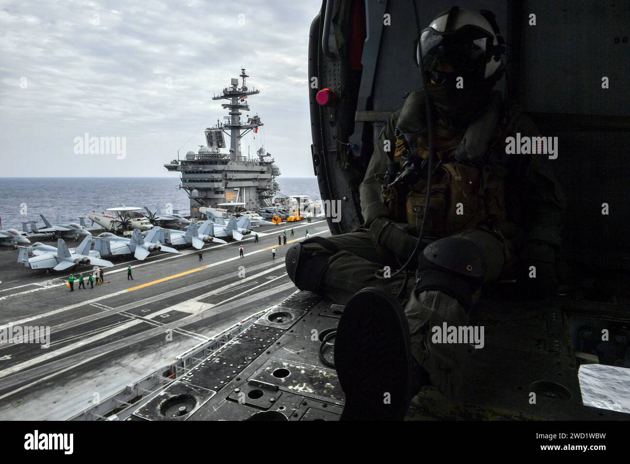 Naval Air Crewman sits in an MH-60S Sea Hawk helicopter while taking from the flight deck of USS Theodore Roosevelt. Stock Photo