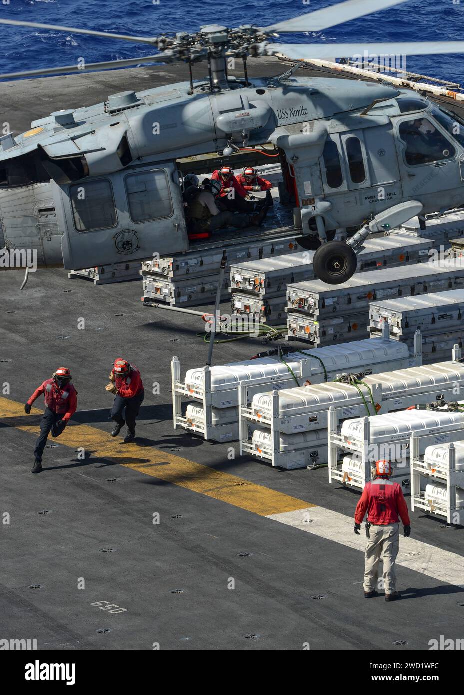 Sailors run to the safe area after loading an MH-60S Sea Hawk helicopter with ordnance aboard USS Nimitz. Stock Photo
