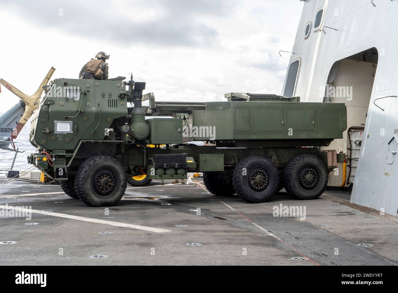 U.S. Marines maneuver a HIMARS vehicle on a flight deck of a ship. Stock Photo