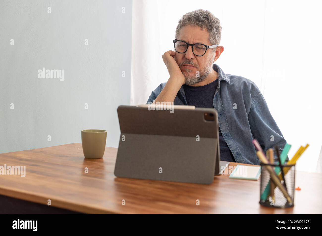 Man focused on digital learning from home, engaging with content on a tablet for personal development. Stock Photo