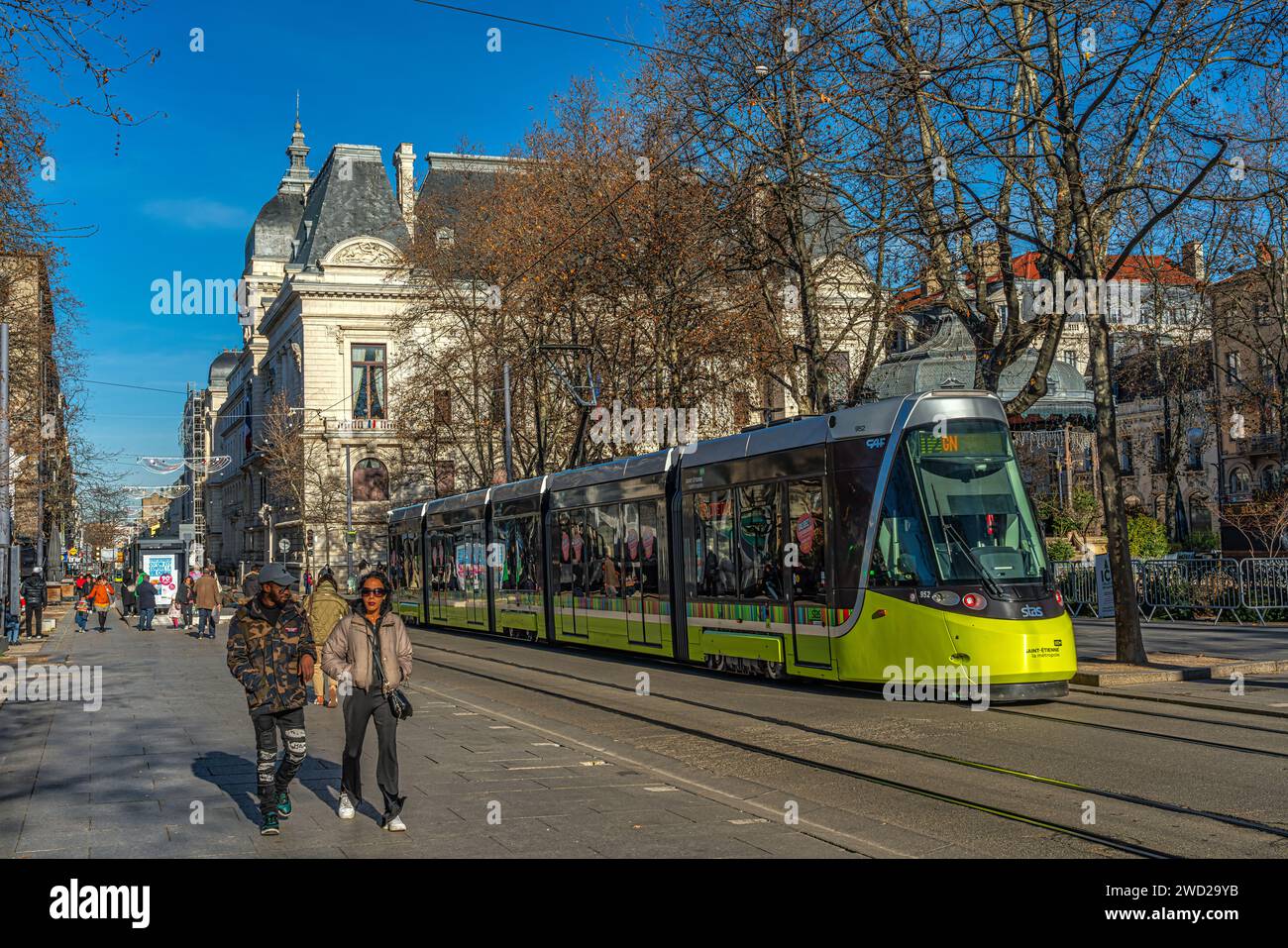 The yellow light rail train in Jean Jaures square on a sunny day with tourists and locals walking. Saint-Étienne, Auvergne-Rhône-Alpes region, France Stock Photo
