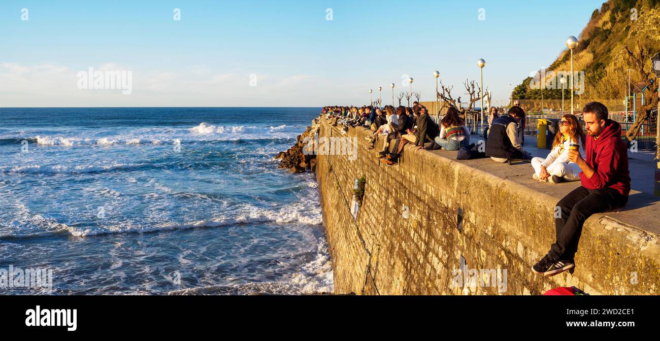 Young people on the Sagüés Wall (El Muro), which provides the perfect setting for enjoying the sunset at Zurriola Beach. San Sebastian, Spain. Stock Photo