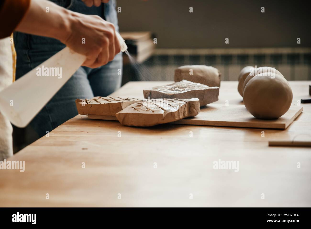 Potter sprinkles water on piece of clay to soften it Stock Photo