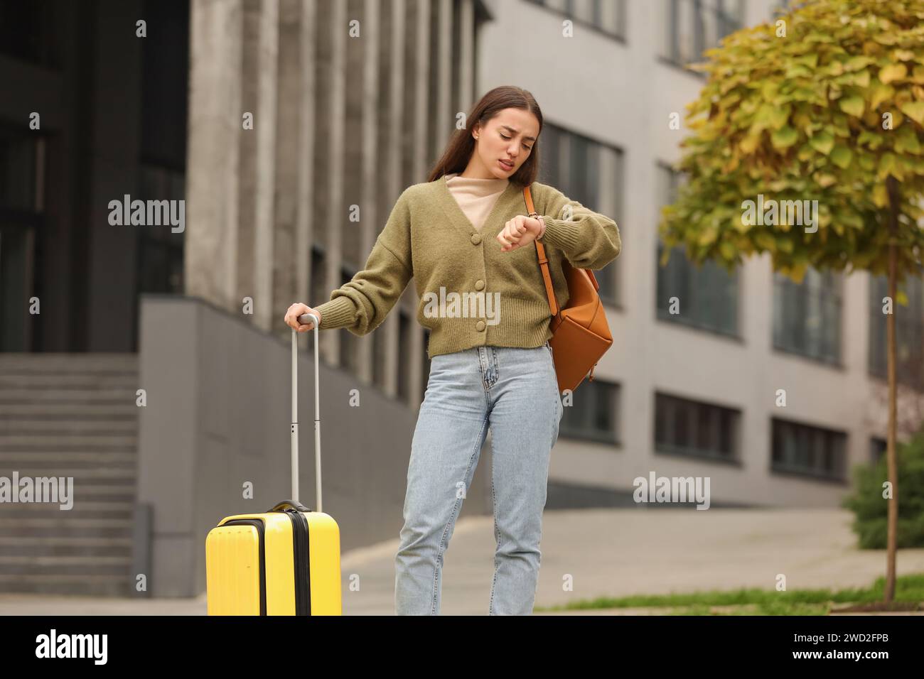Being late. Worried woman with suitcase and backpack looking at watch outdoors Stock Photo