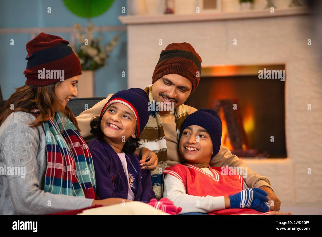 Happy family in winter wear spending time together at weekend holidays near fireplace at home - concept of relationship bonding, parenthood and Stock Photo
