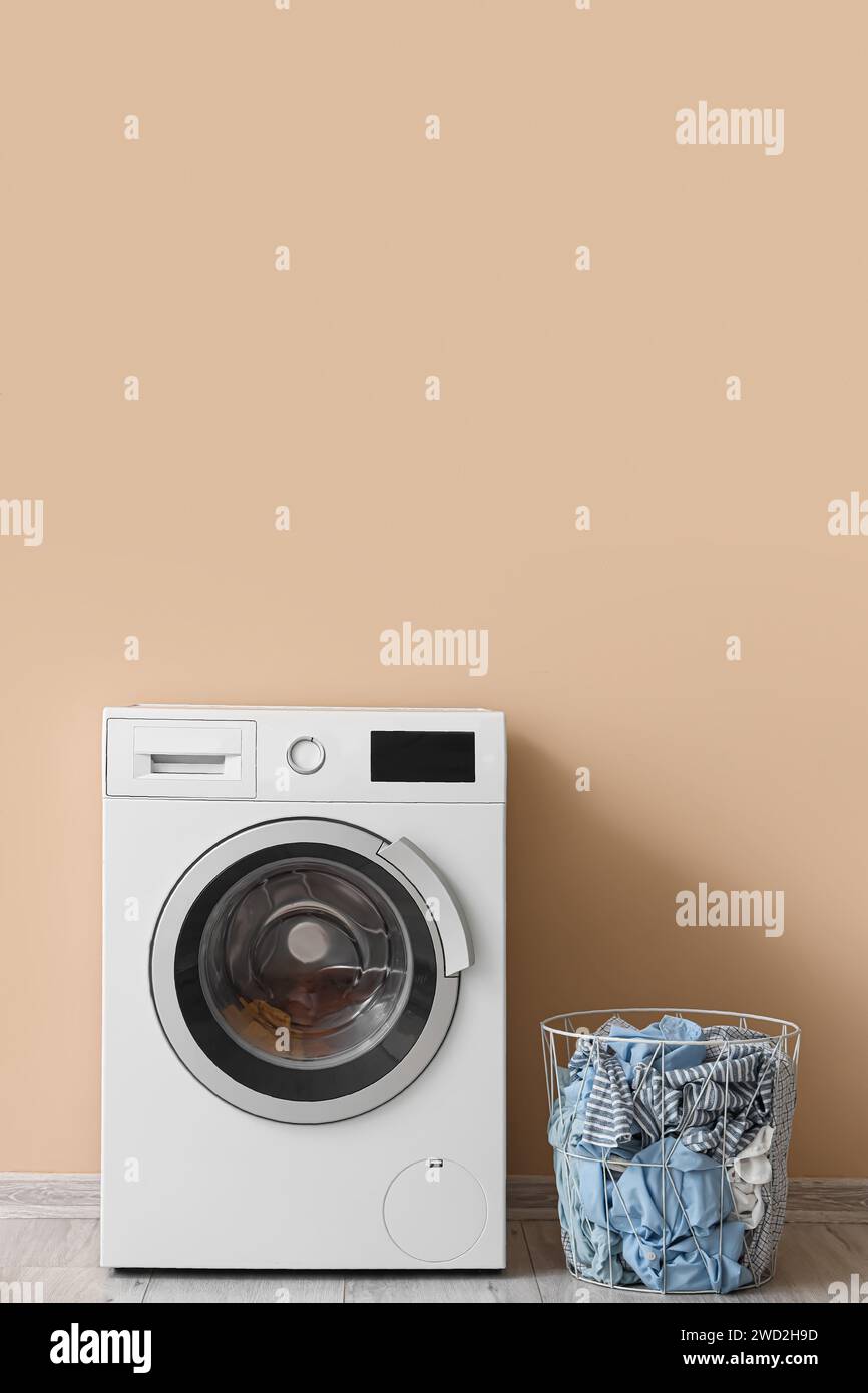 Modern washing machine with laundry basket near beige wall Stock Photo ...