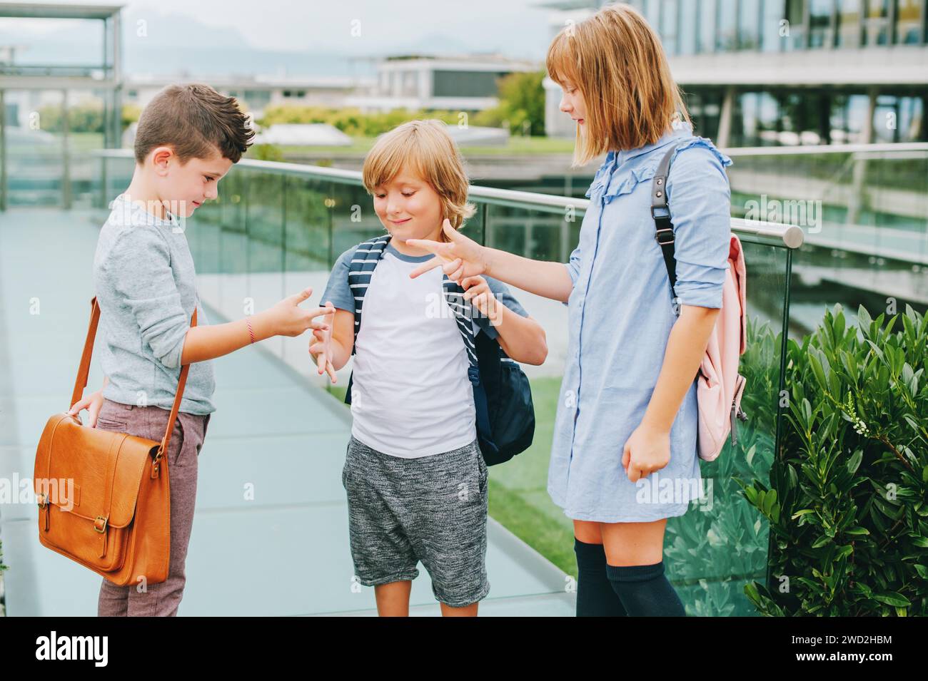 Group of 3 kids playing Rock, Paper, Scissors game on schoolyard. Back to school concept, fashion for children Stock Photo