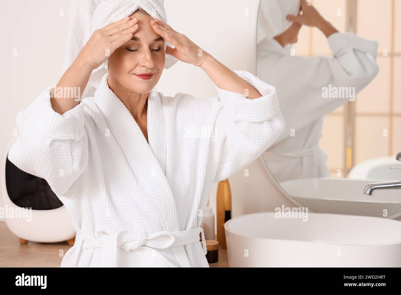 Mature woman doing face building exercise after shower in bathroom