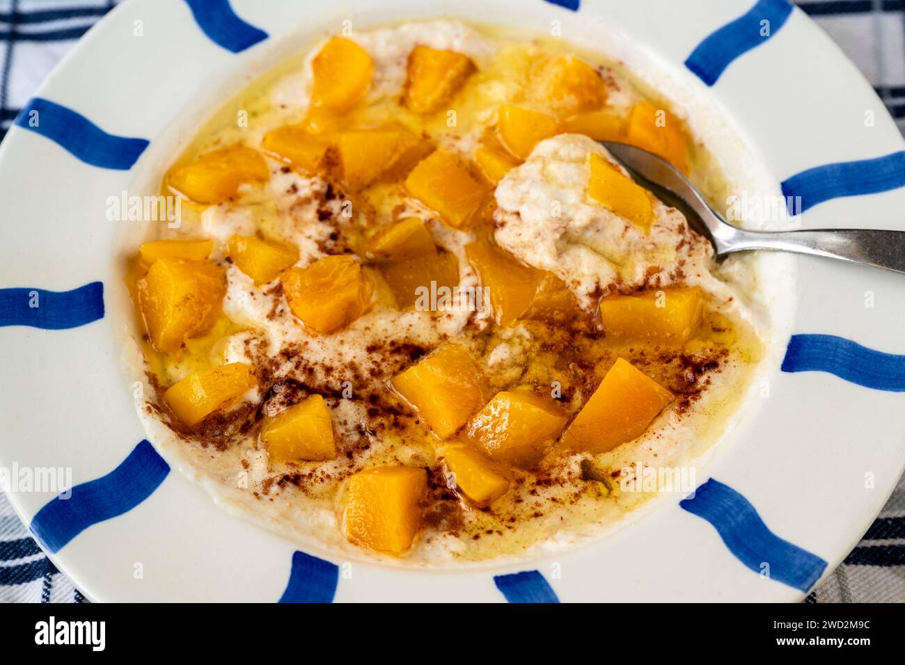Almond porridge with sliced peach, cinnamon and honey in blue striped plate, closeup. Stock Photo