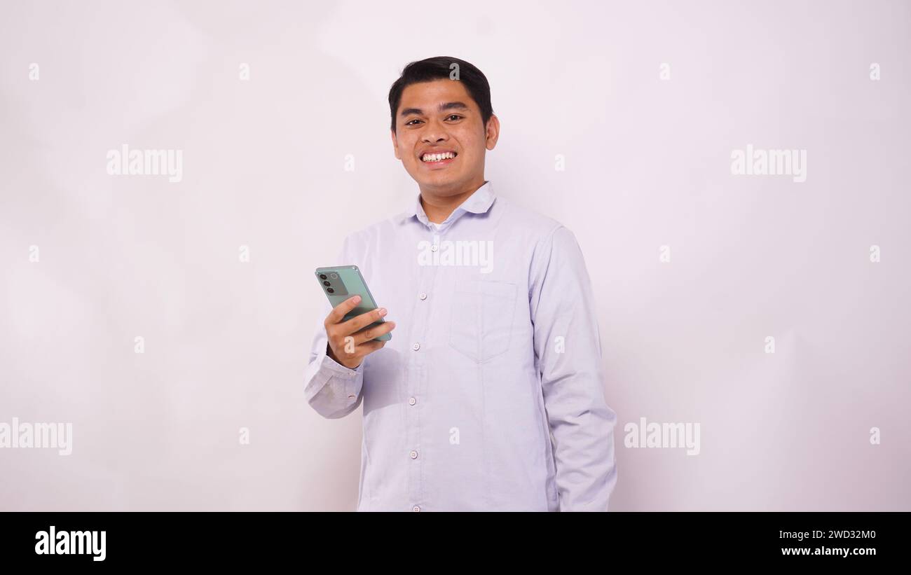Young Asian man holding mobile phone showing enthusiastic expression on white background Stock Photo