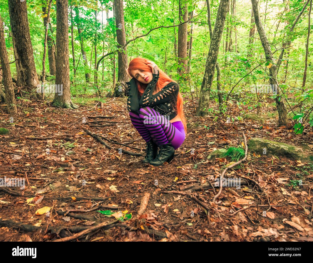 A red-haired young woman in purple striped leggings posing in the green forest Stock Photo