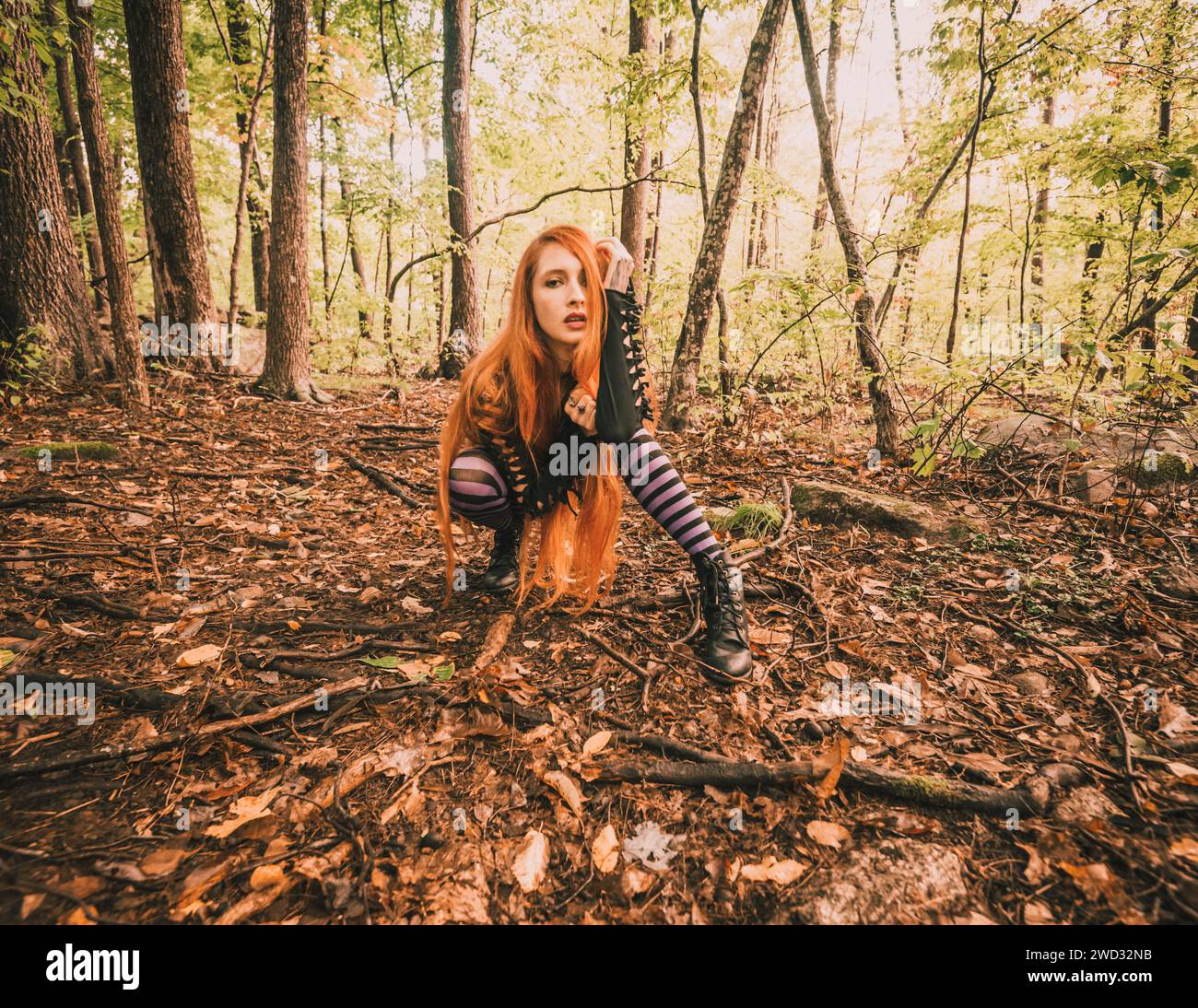 A red-haired young woman in purple striped leggings posing in the forest Stock Photo