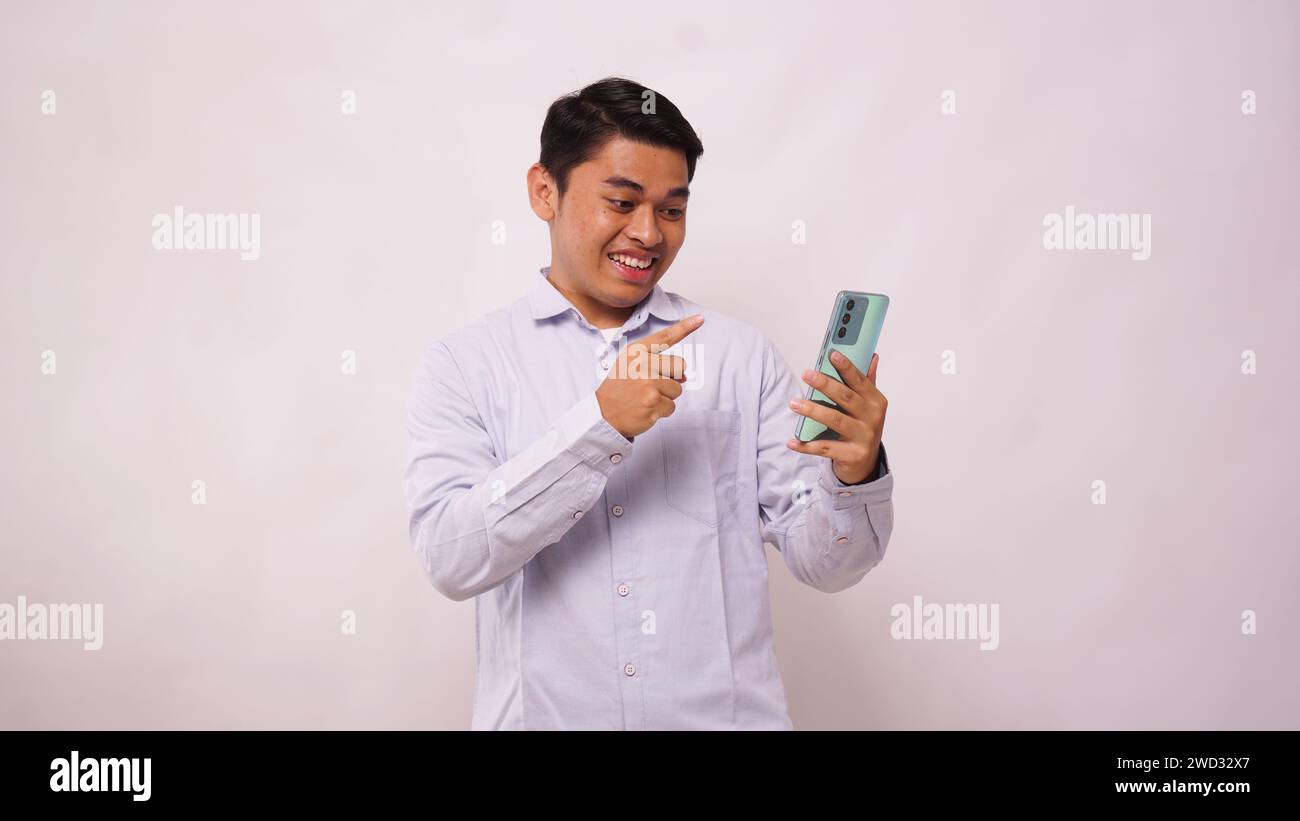 Asian man clenched fist showing excitement when looking to his phone on white background Stock Photo