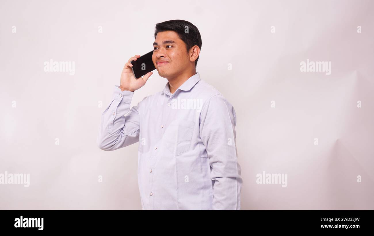 Asian man smiling at camera while answering a mobile phone call on white background Stock Photo