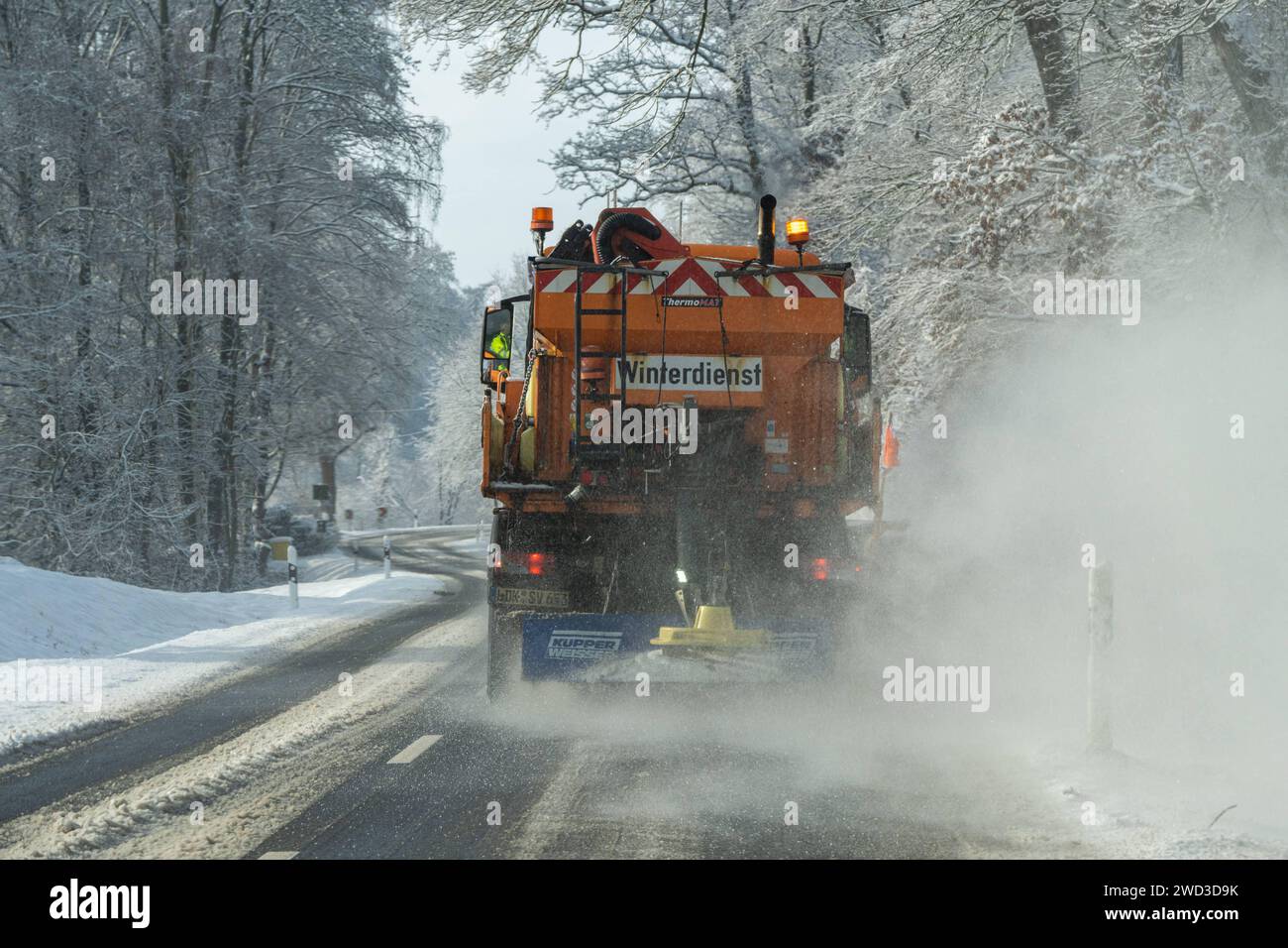 Winterdienst in Aktion: Schneeräumung und Salzstreuung 18.01.2024, Selters: Symbolfoto, Illustrationsbild, Symbolbild, Illustrationsfoto Winterdienst in Aktion: Schneeräumung und Salzstreuung Dieses Bild zeigt ein Winterdienst-Fahrzeug in Aktion, gesehen durch die Frontscheibe eines anderen Fahrzeugs. Der Winterdienst-LKW schiebt Schnee und streut Salz auf die Straße. Die Aufnahme wurde mit Langzeitbelichtung gemacht, wodurch die schneebedeckten Bäume am Rand der Straße wie vorbeifliegend erscheinen. Der Himmel ist teilweise blau und sonnig, was eine schöne und stimmungsvolle Winterkulisse erz Stock Photo