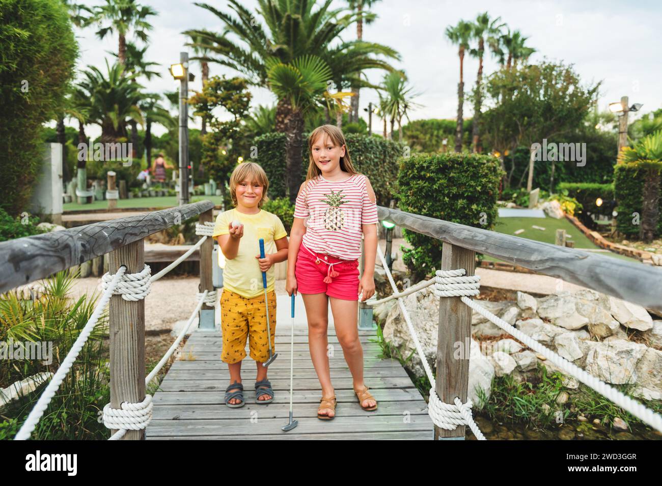 Group of two funny kids playing mini golf, children enjoying summer vacation Stock Photo