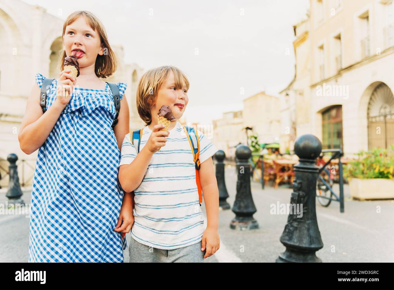 Two funny kids tourist on the street of old european city, children enjoying summer vacation on south of France. Little boy and girl eating chocolate Stock Photo