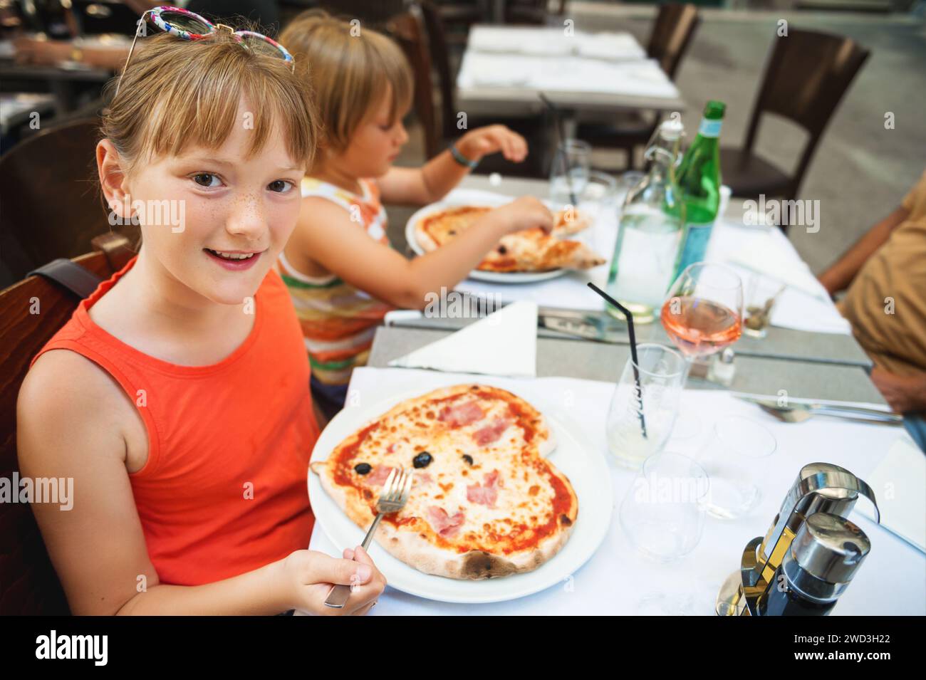 Happy little girl eating kid's pizza in the restaurant. Menu for children, heart shaped italian pizza Stock Photo