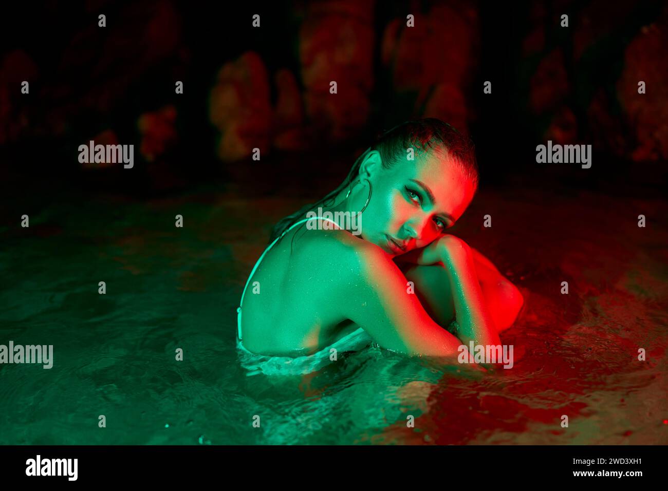 Woman immersed in water under red and green lights, night time, emotion expression, potential metaphor for struggle with depression or psychological Stock Photo