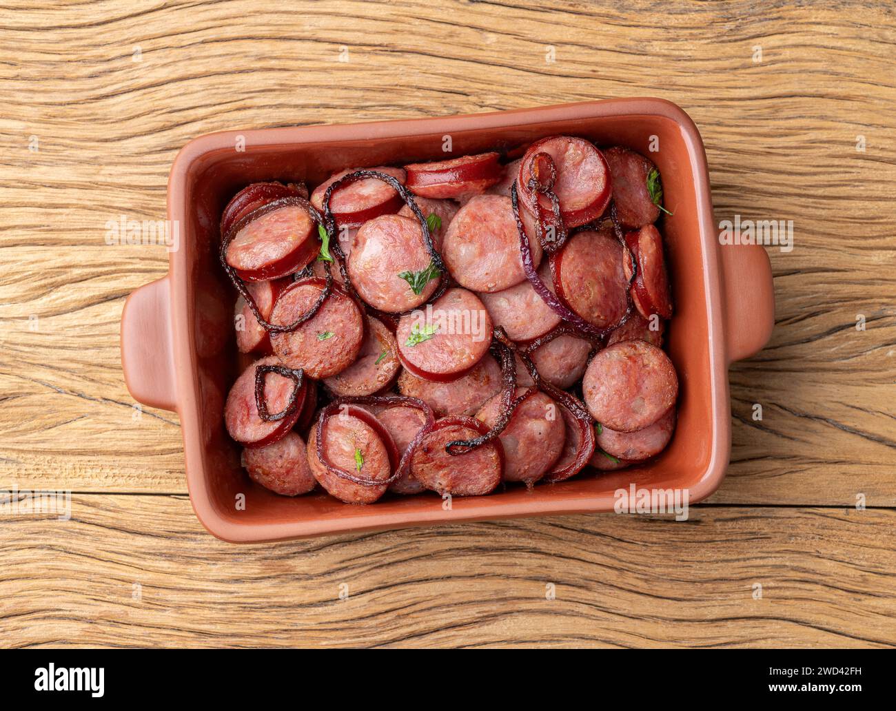 Grilled calabrese sausage portion with onion over wooden table. Stock Photo