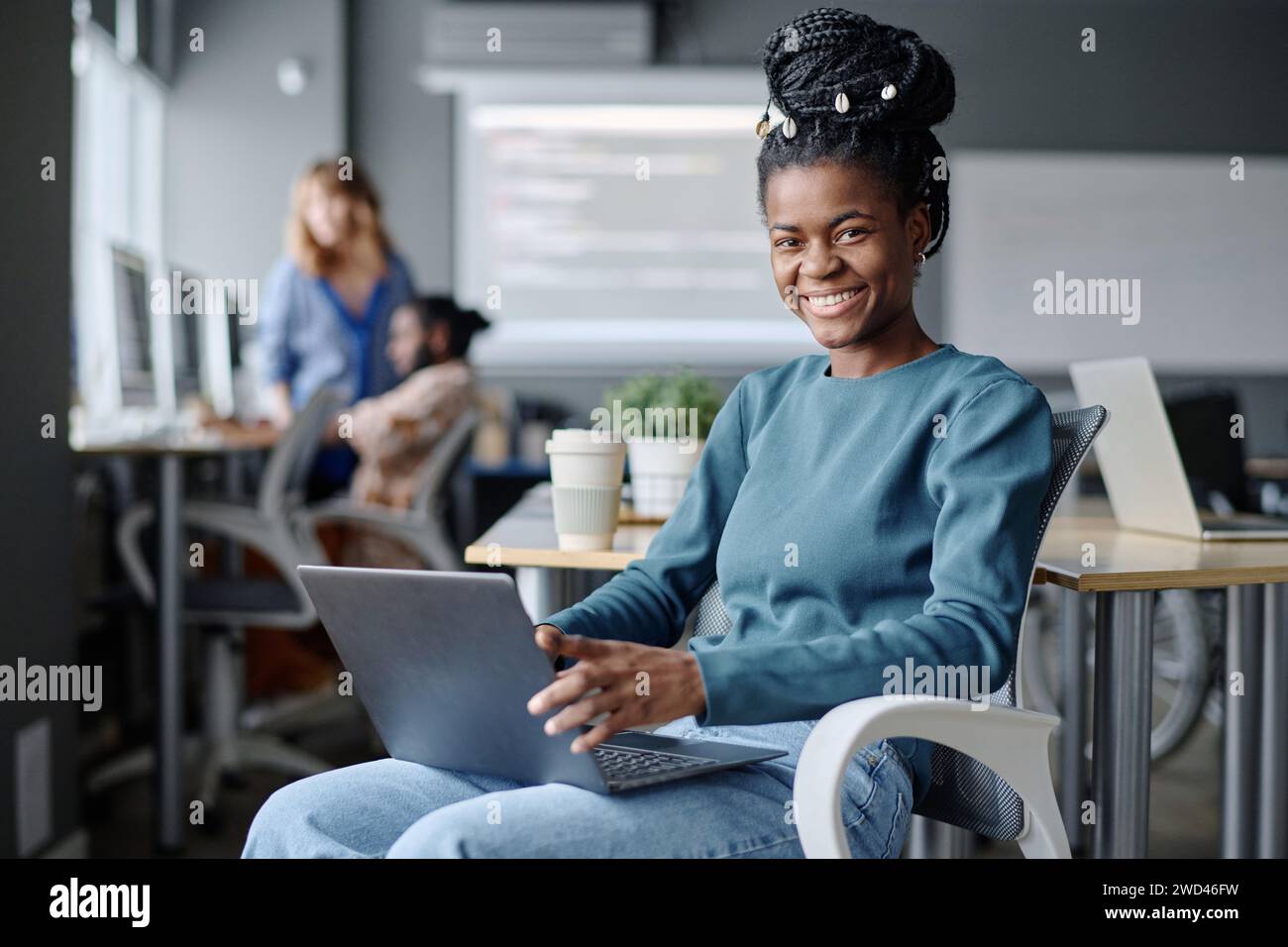 Young female african american coder sitting on chair with laptop on her