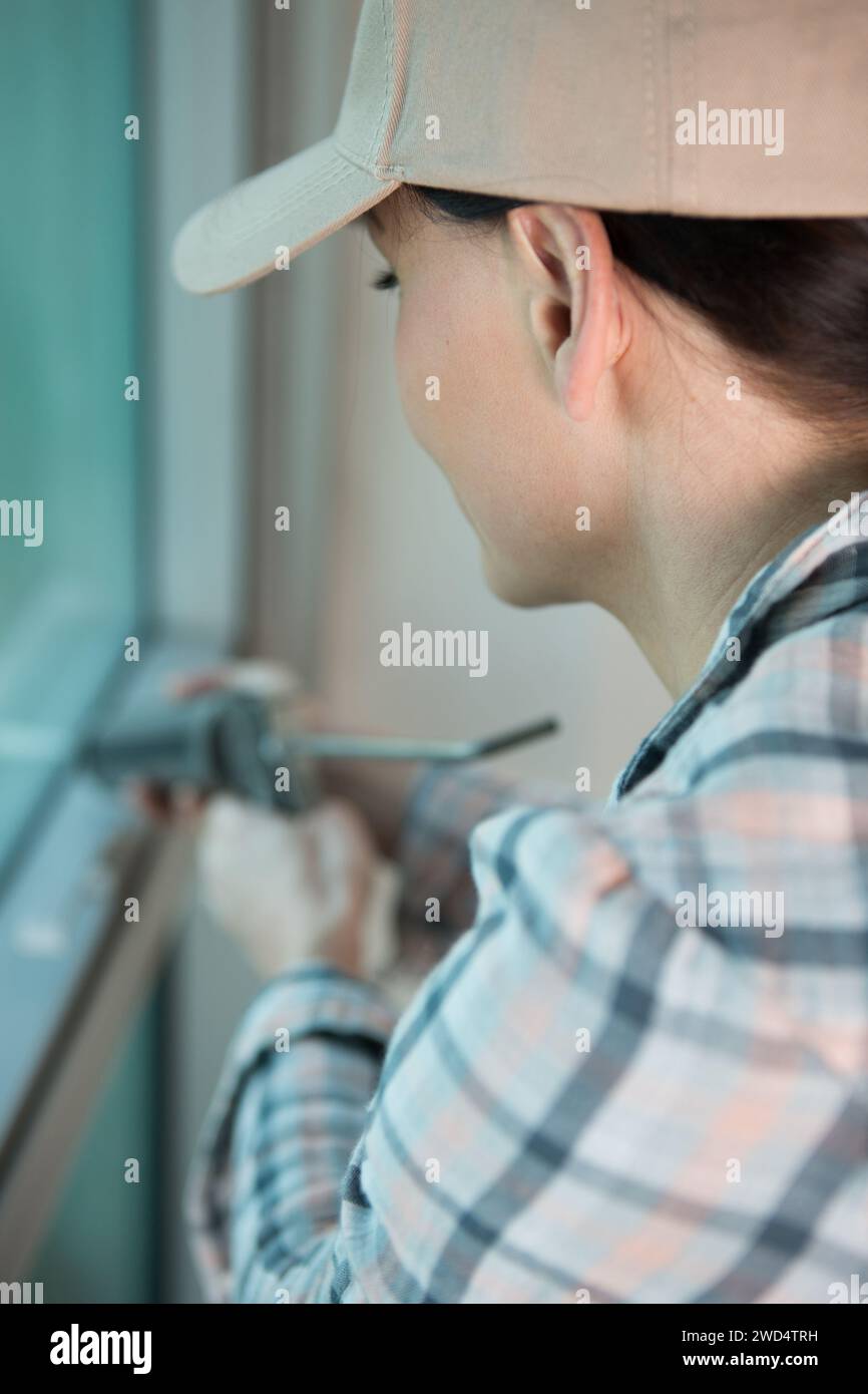 beautiful female construction worker using caulking gun Stock Photo