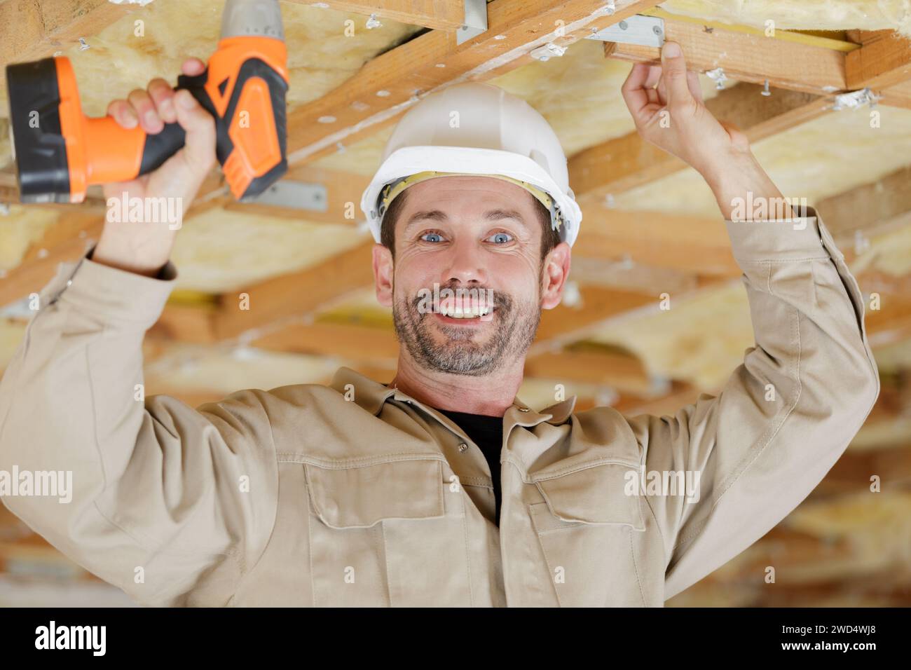 smiling handyman using cordless drill to the ceiling Stock Photo