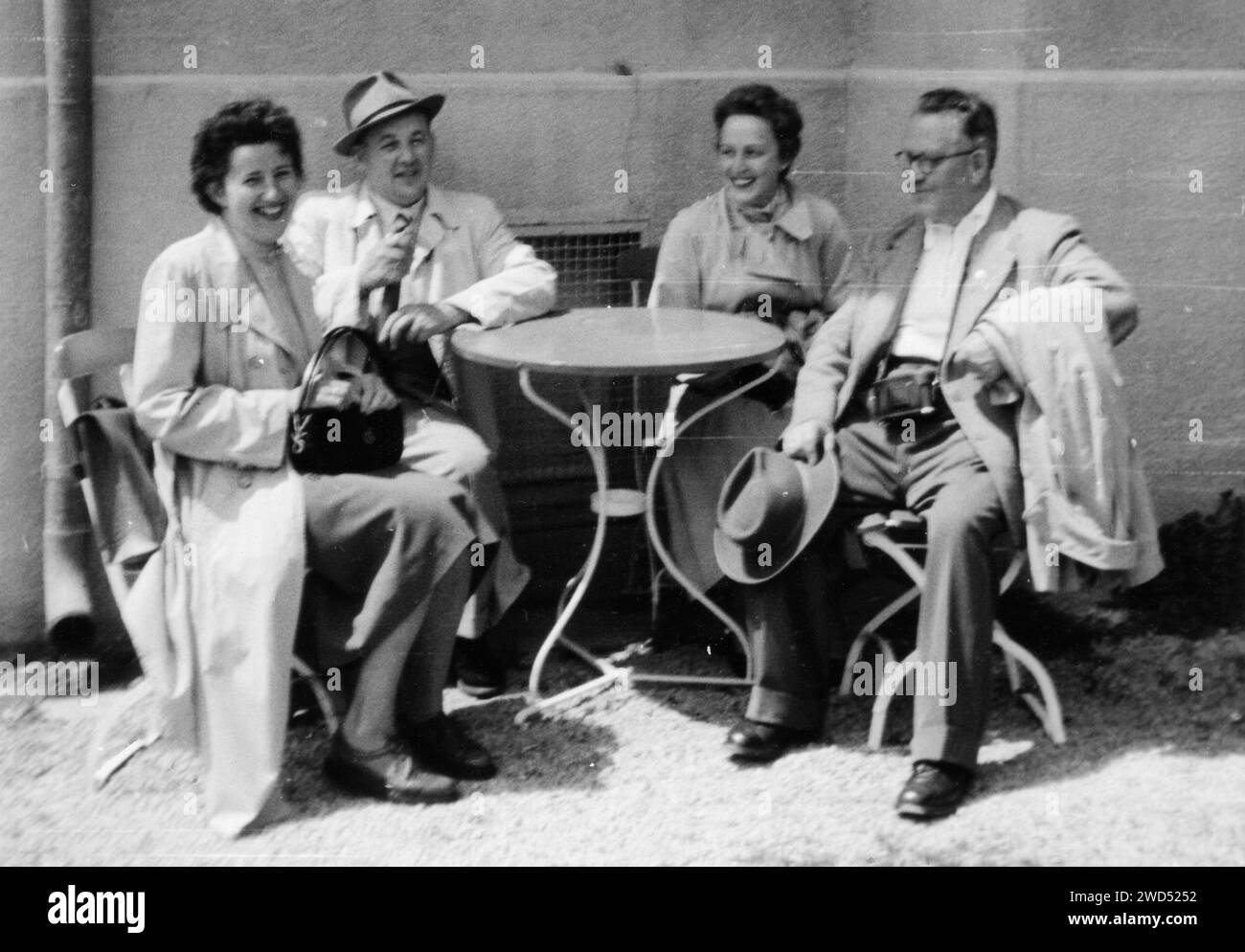 An antique photo with shows two elderly Caucasian family couples posing, sitting on a chair in front of the table on the street. Photographer Lorch. L Stock Photo