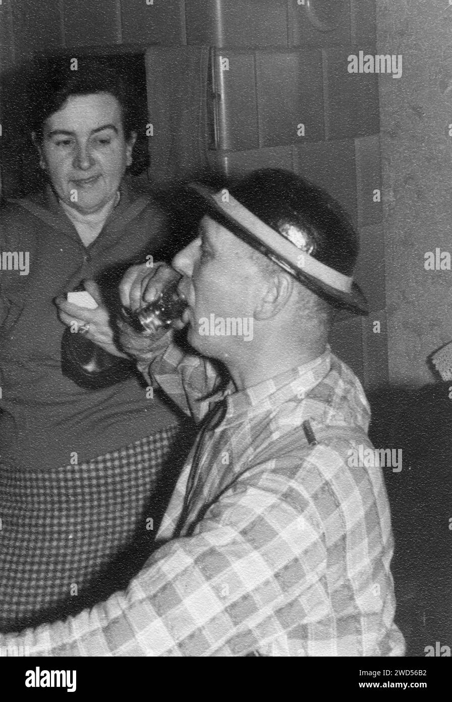 An antique photo with shows a man in a checkered shirt and hat drinks