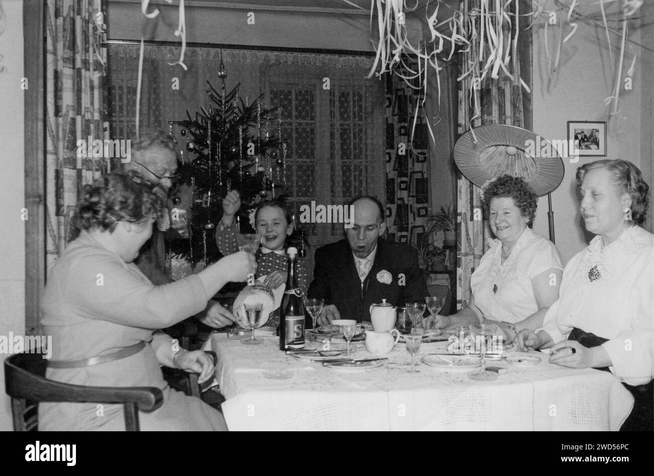 An antique photo with shows a company of men, women and girls6 celebrating Christmas at a table against the backdrop of a Christmas tree. Landau in de Stock Photo