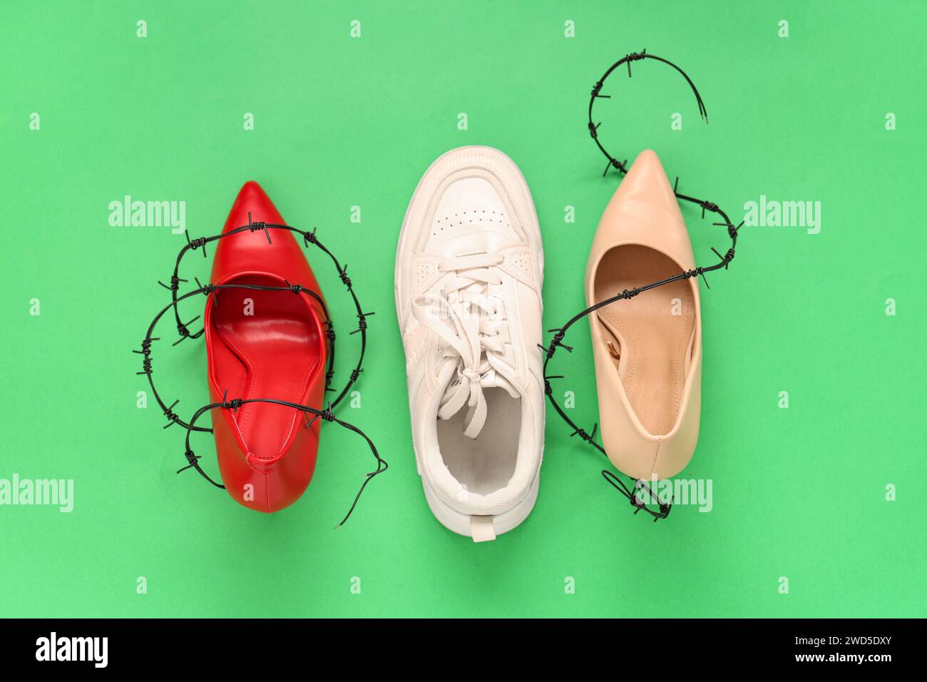 Sneaker and highheeled shoes wrapped in barbed wire on green
