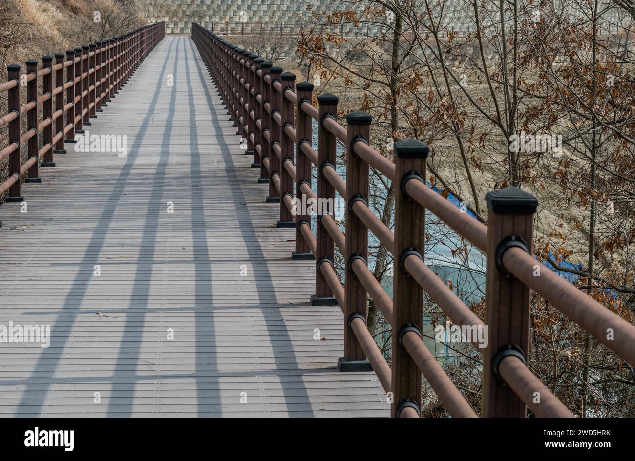 Wooden pedestrian bridge with shadow of railing in mountainside park on ...
