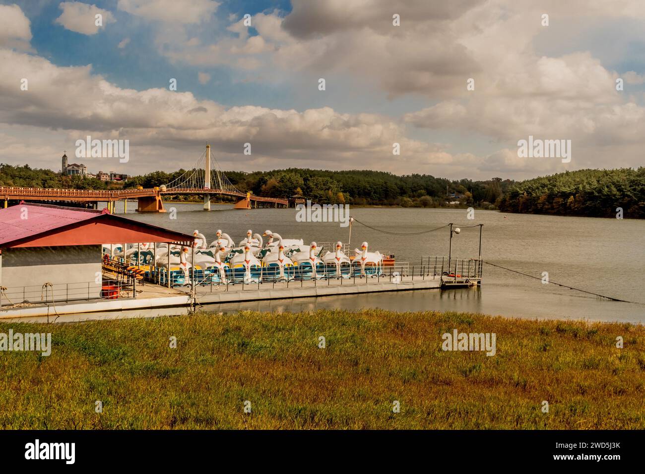 Paddle boats docked at boathouse on lake with long wooden footbridge in