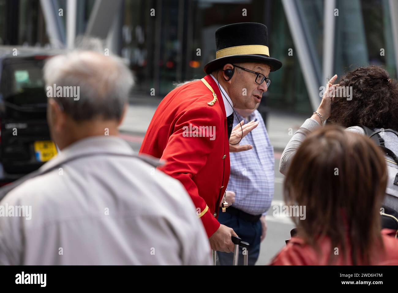 A concierge dressed in smart traditional red uniform outside the Rubens Hotel in Victoria, Central London. He is helping a passenger into a black taxi Stock Photo
