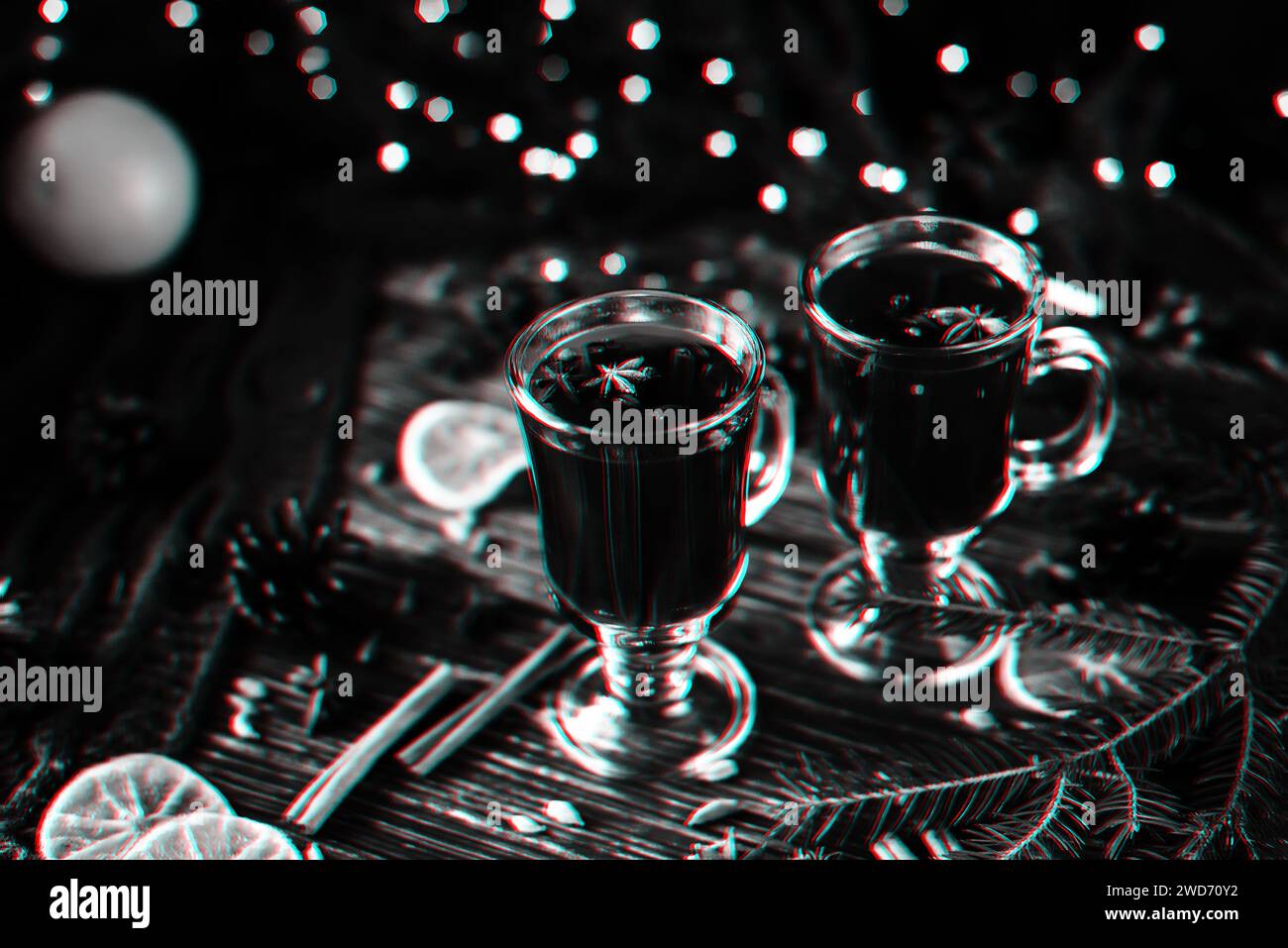 glasses with mulled wine on a wooden table decorated with a Christmas tree and Christmas lights. Black and white monochrome photography with 3D glitch Stock Photo