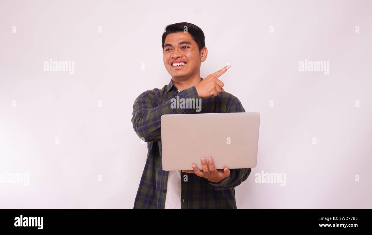 Asian man holding laptop and pointing up side agains gray background Stock Photo