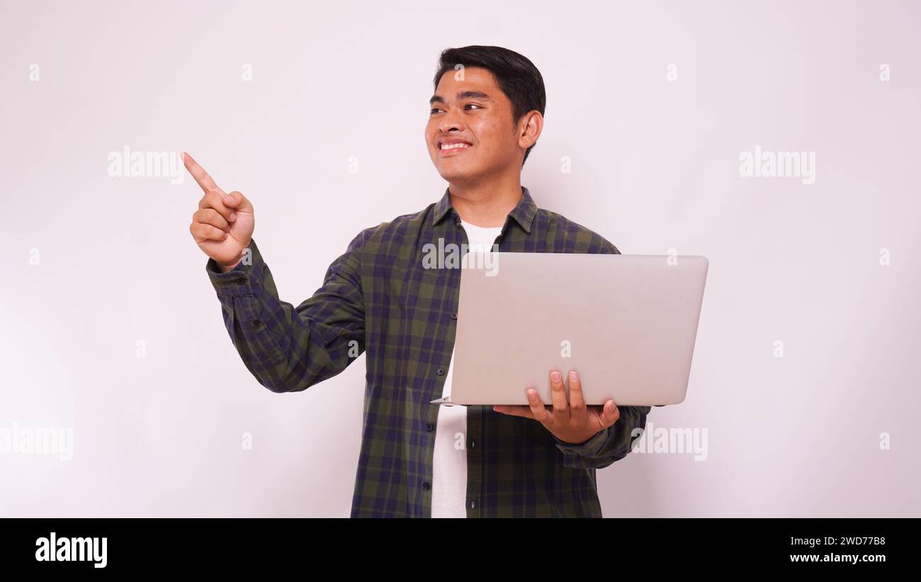 Asian man holding laptop and pointing up side agains gray background Stock Photo