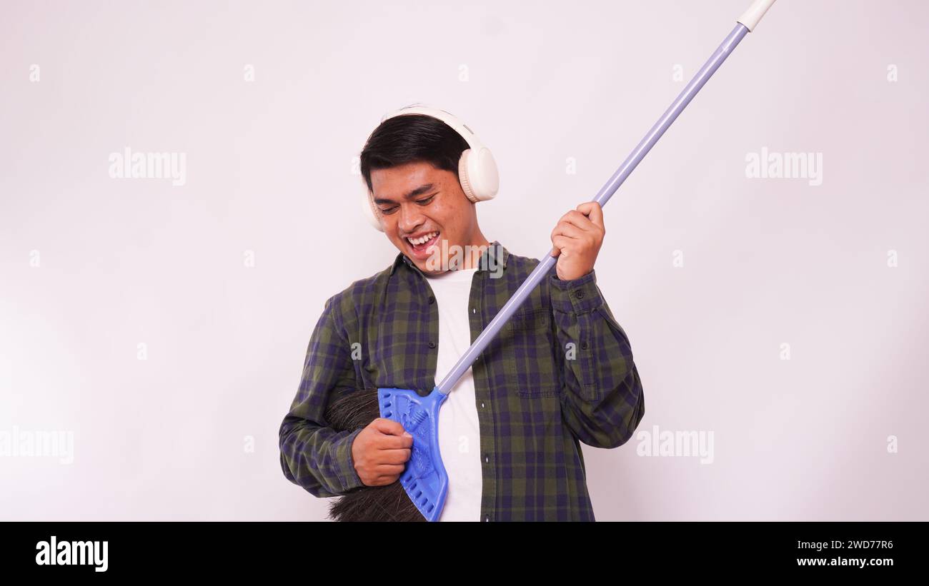 Asian man listening music with headphone and playing guitar with broom against white background Stock Photo