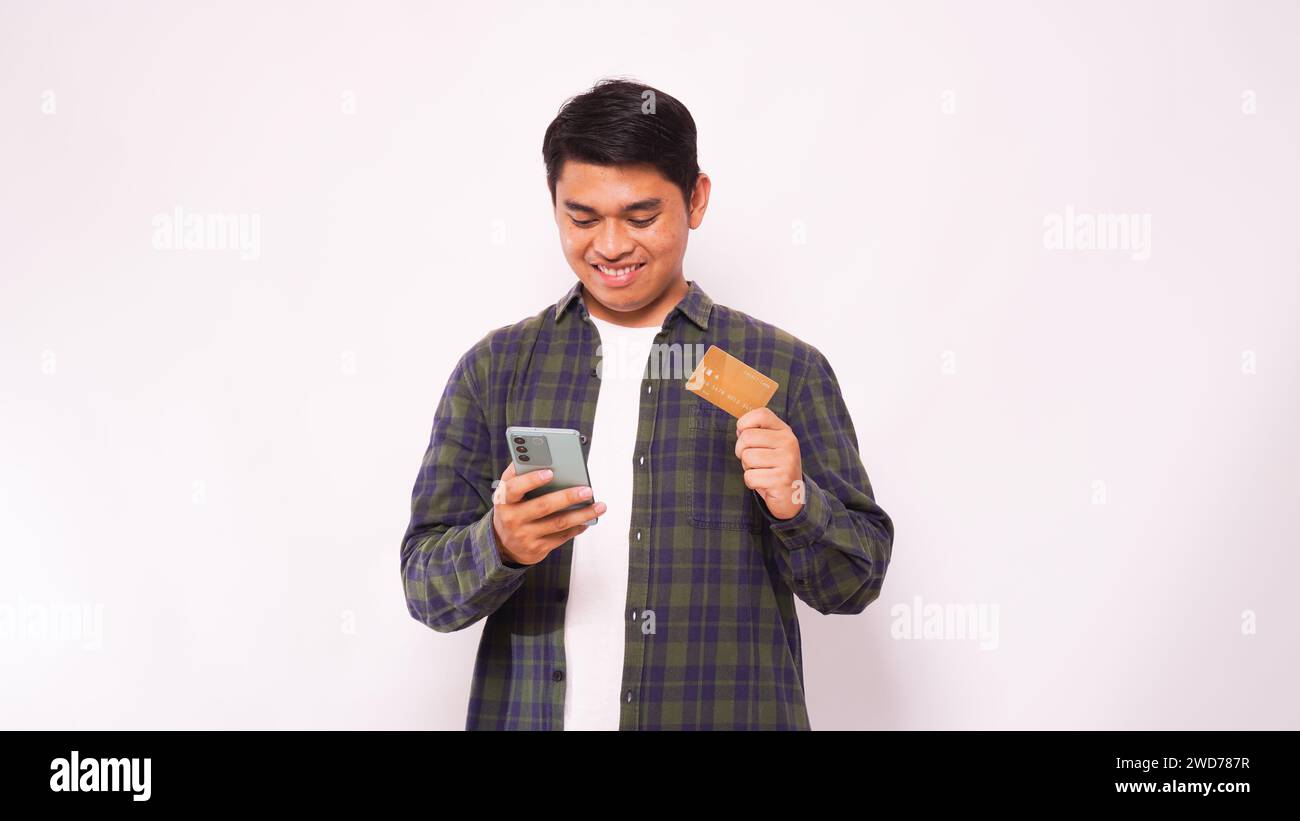 Adult Asian man smiling while holding blank credit card and mobile phone over gray background Stock Photo