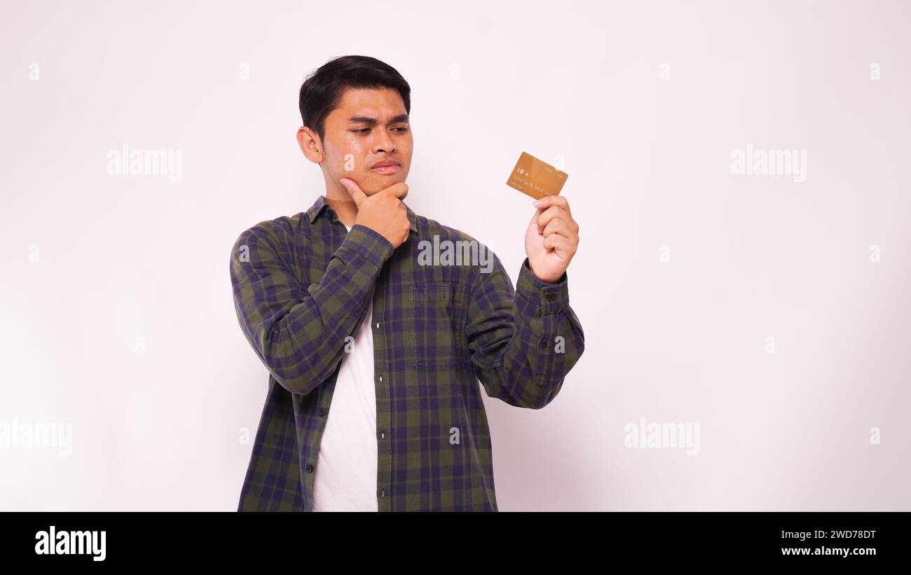 Young Asian man showing confused expression when looking to credit card that he hold over white background Stock Photo
