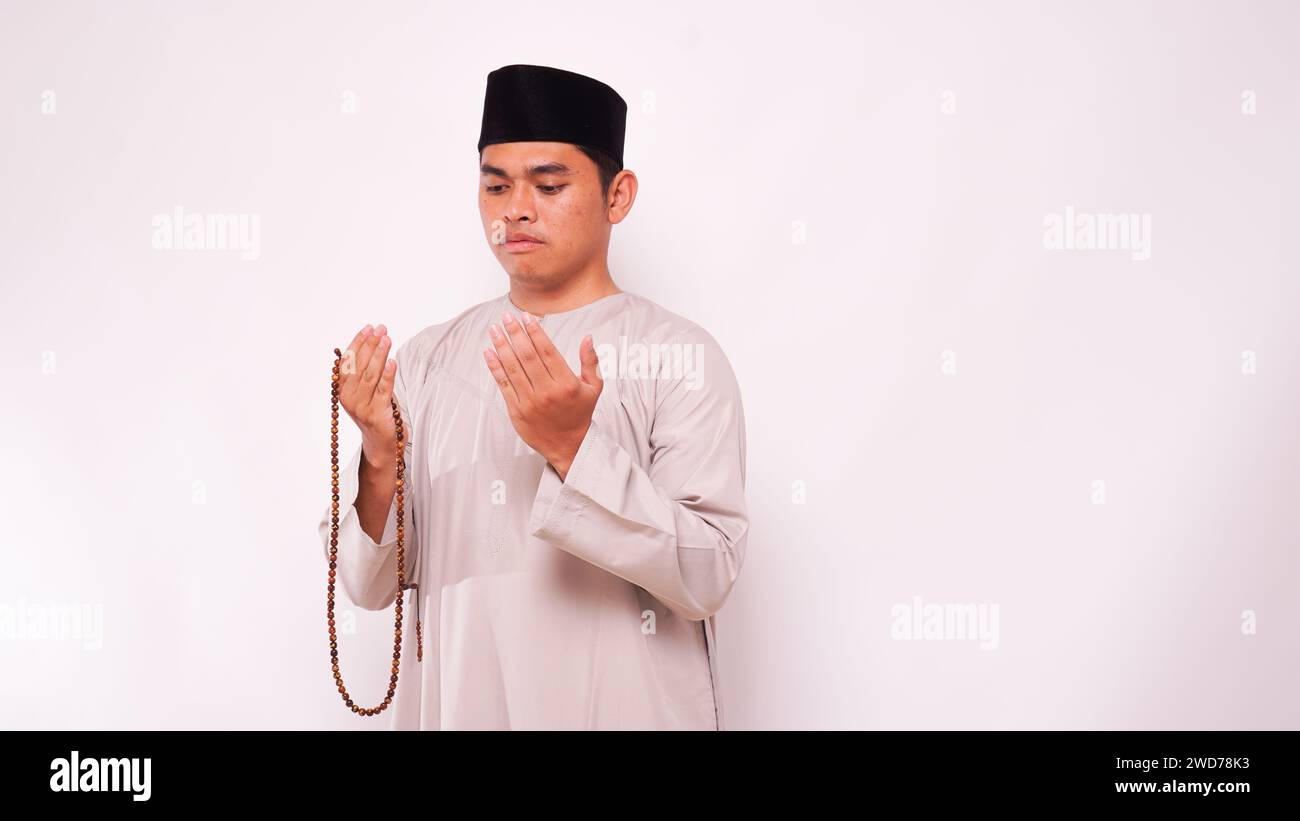 Asian muslim man holding prayer beads and praying against white background Stock Photo