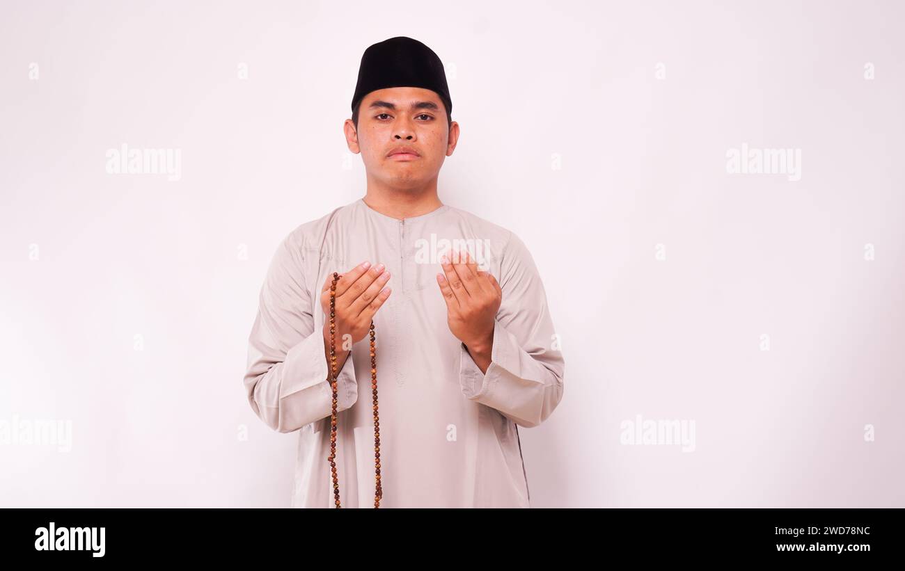 Asian muslim man holding prayer beads and praying against white background Stock Photo